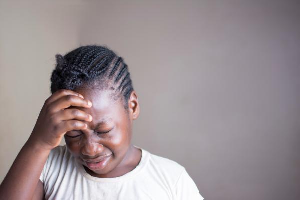 a young black girl, holding her head in pain